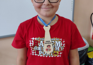 Uśmiechnięty chłopiec w czerwonej koszulce i w okularach w krawacie z napisem "Super chłopak."